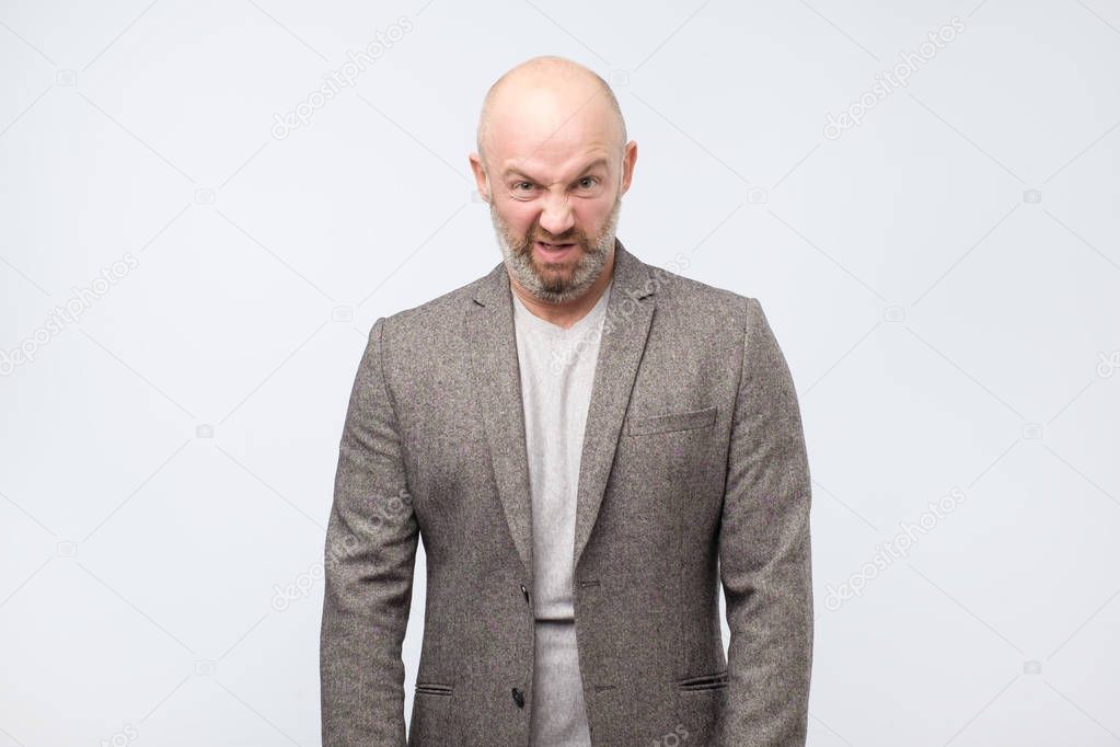 Mature suspicious mature man isolated against white studio background. His face is in disgust grimace.