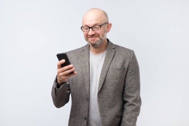 Olgun Avrupa beyaz adam dikkatle gülümseme ile akıllı telefon ekranına bakarak o tutuyor. hoş bir haber onun kız arkadaşından aldığı
