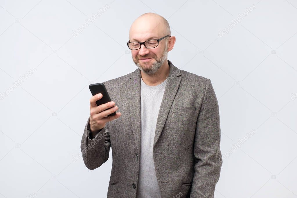 Mature european caucasian man looking attentively with smile at screen of smartphone he is holding. he received a pleasant news from his girlfriend