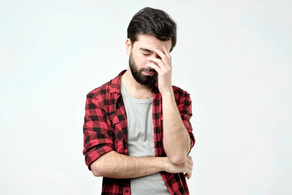 Xhausted ung man som täcker ansiktet med handen stående mot grå bakgrund — Stockfoto