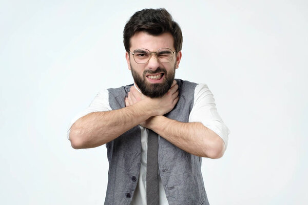 Young hispanic man grabs his throat with both hands and squints intensely from the pain in his throat. He lost all his money