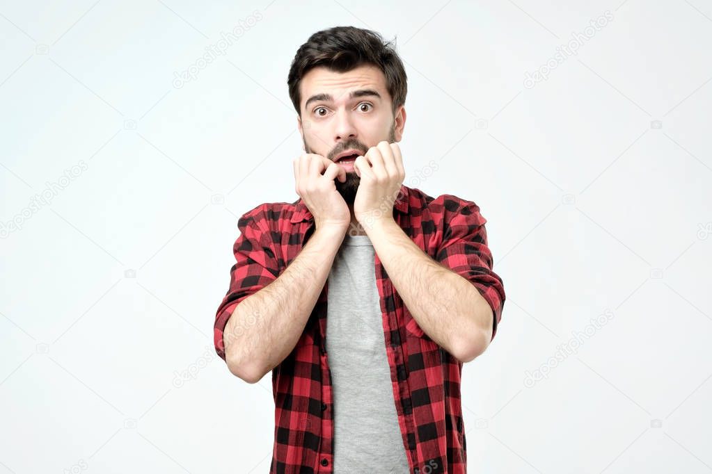 Young man covering mouth with hands and round eyes experiencing deep astonishment and fear