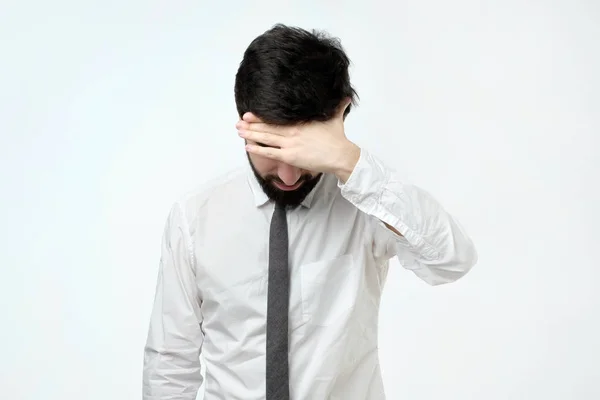 Erschöpfter junger Mann verdeckt Gesicht mit der Hand, während er vor grauem Hintergrund steht — Stockfoto