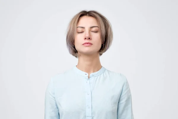 Joven mujer europea con camisa azul cerrando los ojos. No hay emoción en su cara . — Foto de Stock
