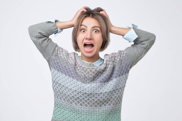 Потрясенная молодая женщина с руками на голове, стоящими и кричащими
