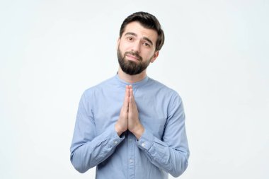 Dua elinde tutan ve kamera hopefu bakan mavi gömlekli adam
