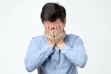 Gri arka plan karşı dururken elinizle yüzünü kaplayan adam