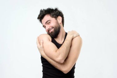 Kendini kucaklayan süre zevkle gülümseyen neşeli İspanyol yakışıklı genç