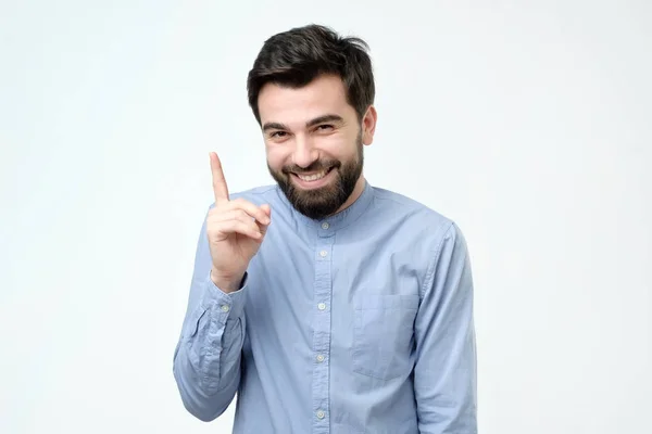 Man in blauw shirt omhoog met zijn vinger geïsoleerd op een grijze achtergrond. — Stockfoto