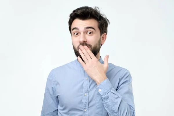 Ood looking hispanic young man in blue shirt covering mouth with hand — Stock Photo, Image