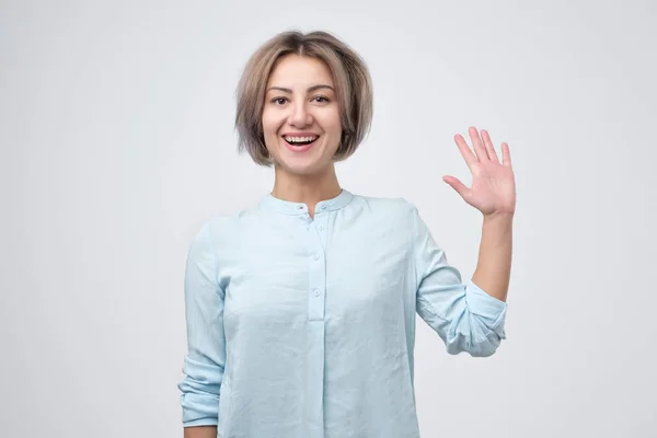 Barátságos európai női vállalkozó, mosolyogva, miközben hullámzó emelt palm — Stock Fotó