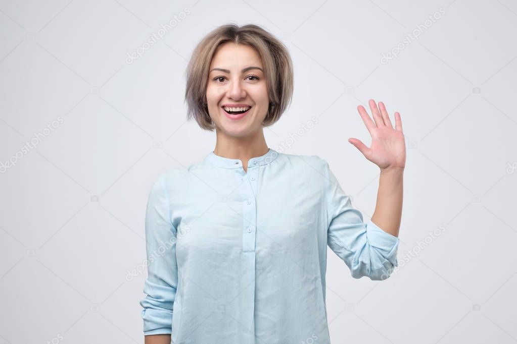 Friendly european female entrepreneur, smiling broadly while waving raised palm