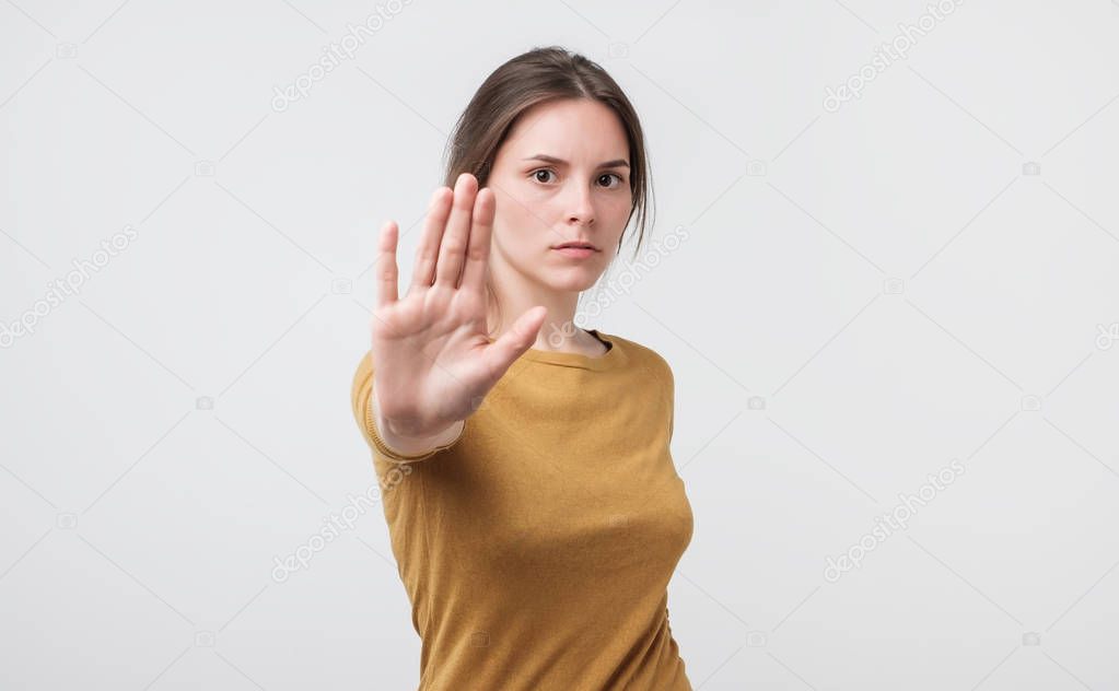 Serious young european woman standing with outstretched hand showing stop gesture isolated over white background