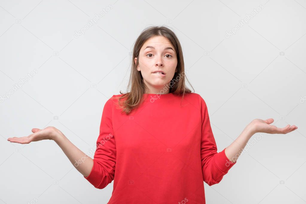 Clueless puzzled woman in red sweater with widely opened eyes having hesitation shrugging her shoulders expressing uncertainty. Nobody cares about it
