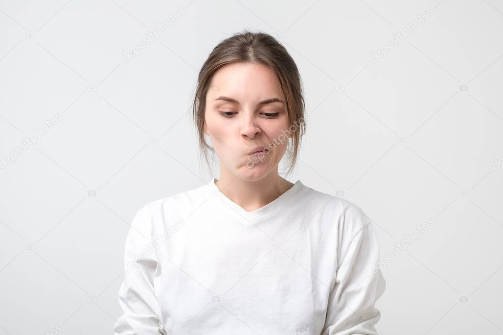 Cute girl looking away, having doubtful and indecisive face expression, pursuing her lips as if forbidden to say anything. Confused young female at studio