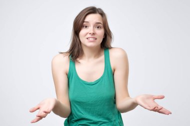 Gri arka plan üzerinde izole omuzlarında shrugging yeşil giysili hayal kırıklığına uğramış genç kızı. Ne seçmek için bilmiyorum