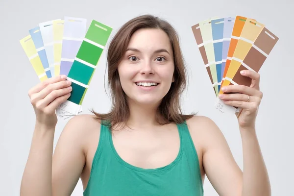 Young european woman in green clothes select a color to paint her wall. She is glad to have such a variety of choice.