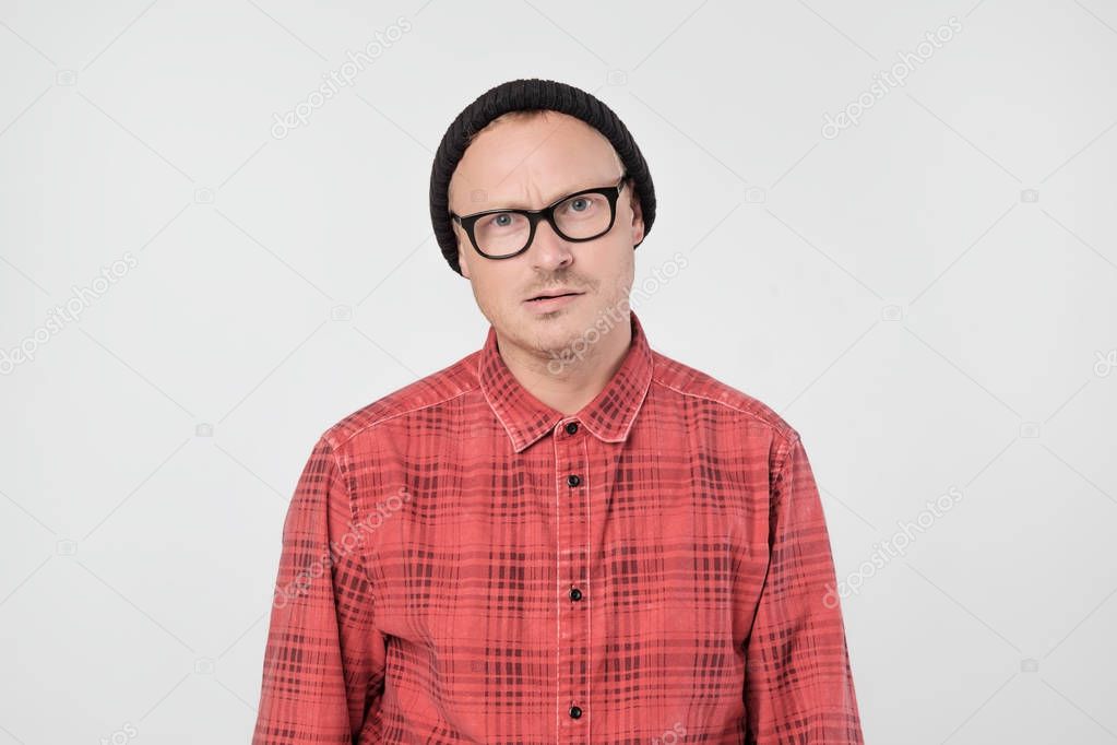 Young european man in red shirt dissatisfied frowns and looks sullenly. He is confused with results of his job.