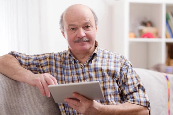 Homem idoso usando tablet sentado em casa . — Fotografia de Stock