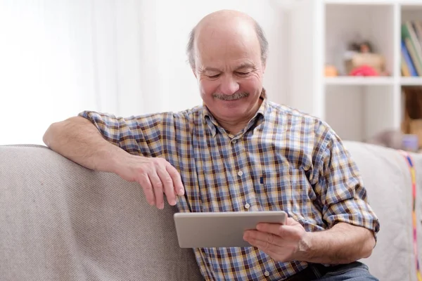 Senior man using tablet sitting at home.