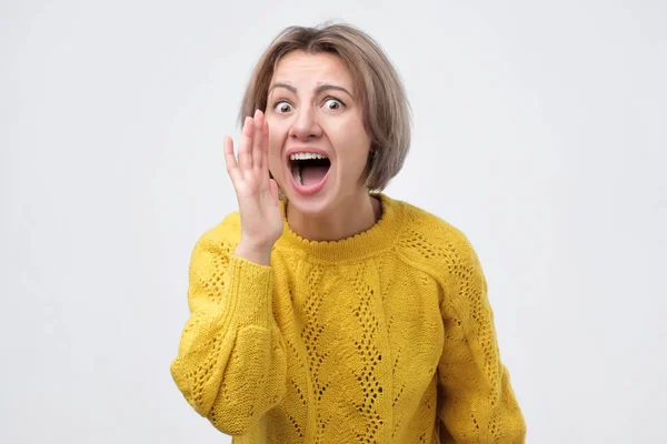 Giovane donna in maglione giallo urlando su sfondo bianco — Foto Stock