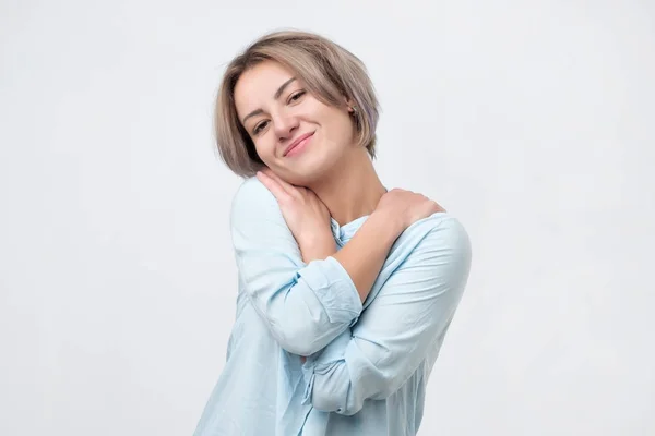 Positiva mujer joven relajada sonriendo con placer, manteniendo los brazos alrededor de sí misma —  Fotos de Stock