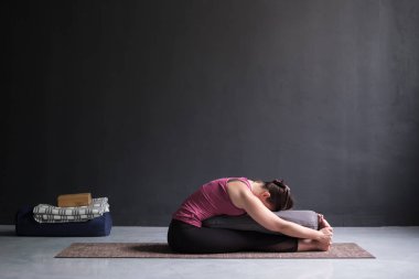 pratik yoga, Seated ileri bend poz yapıyor, bolster kullanarak kadın.