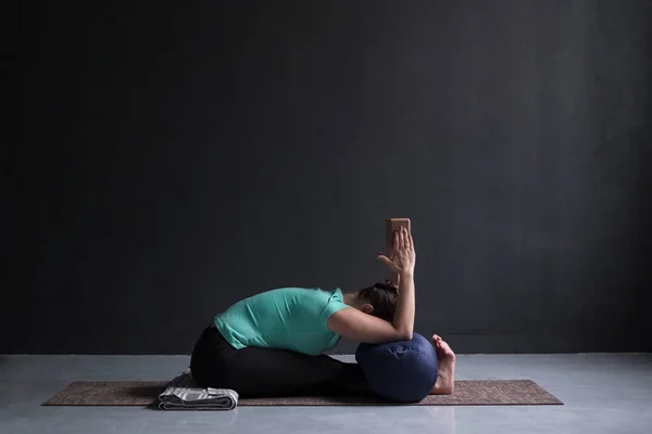 Kvinna som utövar yoga, sittande framåt bend pose, med hjälp av block och bolster — Stockfoto