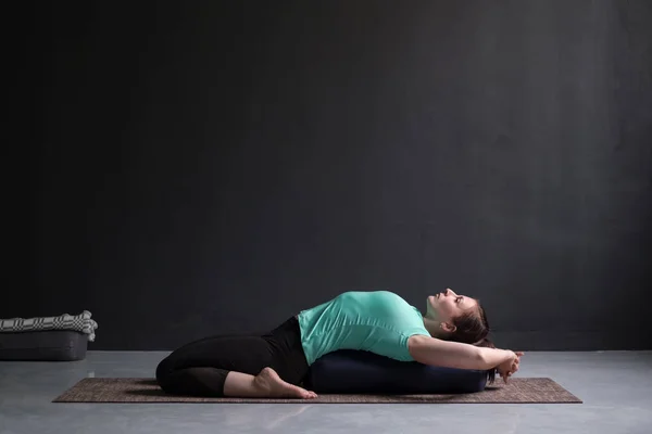 Beautiful athletic girl doing yoga supta virasana asana using bolster — Stock Photo, Image