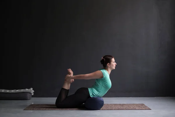 Woman practicing yoga Bow pose, Dhanurasana using bolster. — Stock Photo, Image