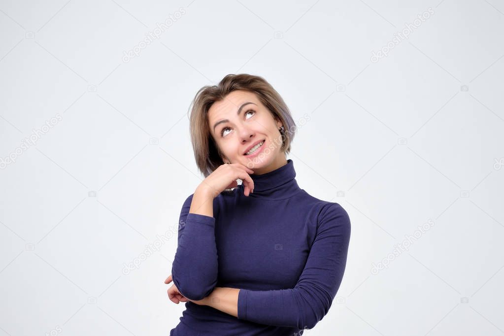Thoughtful and dreamy woman thinking about thing she desire with intrigued and interested expression looking at up over gray background