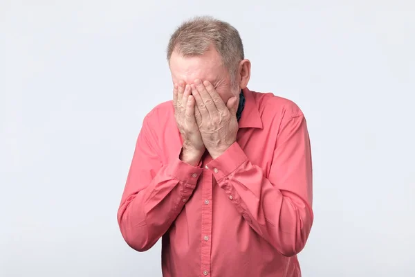 Äldre mannen i röd tröja som täcker hans ögon med händerna — Stockfoto
