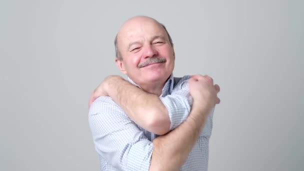 Selbstbewusster älterer lächelnder Mann umarmt sich. — Stockvideo