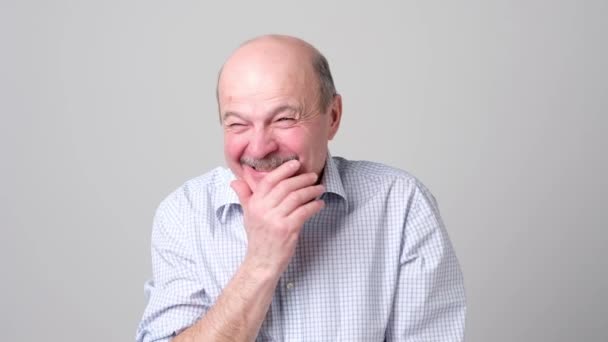 Hombre maduro riéndose y cubriéndose la boca con la mano sobre fondo blanco . — Vídeos de Stock