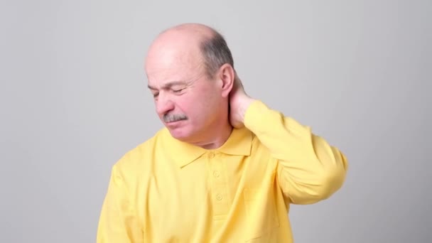 Mature homme en tshirt jaune avec les yeux fermés touchant son cou dans la douleur . — Video