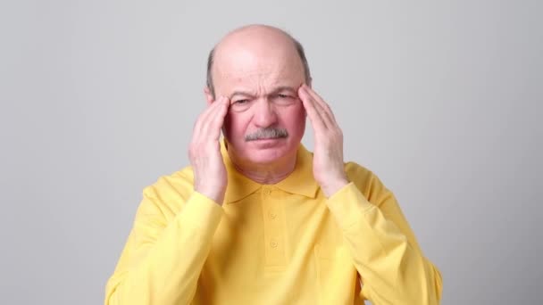 Mature homme en tshirt jaune avec les yeux fermés touchant sa tête dans la douleur . — Video