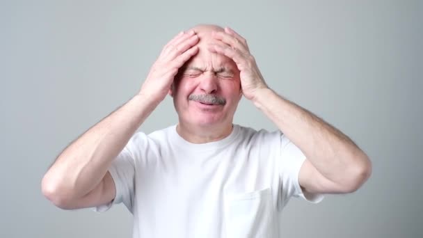 Mature man in white tshirt with closed eyes touching his head in pain. — Stock Video