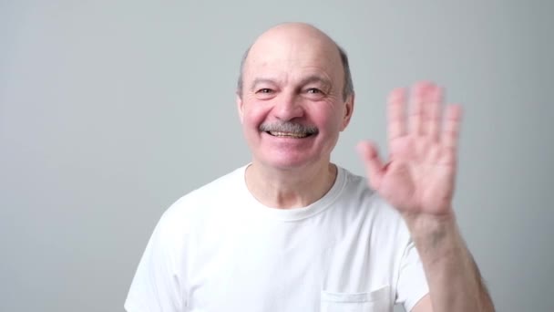 Pensionista europeo renuncia de la mano en gesto de saludo mientras sonríe alegremente . — Vídeo de stock