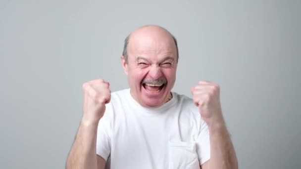 Щасливий лисий старший чоловік святкує свій успіх на сірому фоні . — стокове відео