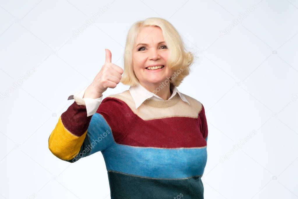 cheerful old woman in colored sweater showing thumbs up gesture