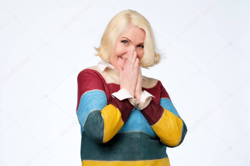 Shy senior woman feeling shy after hearing a compliment posing in studio.