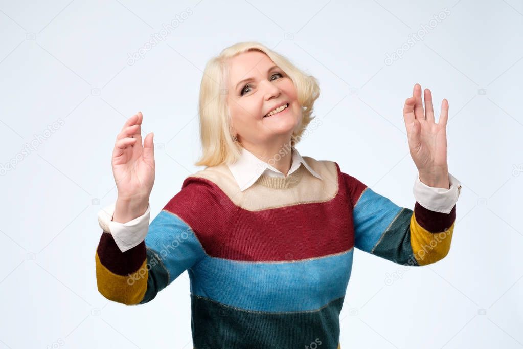 Cheerful aged woman in colored sweater dancing.
