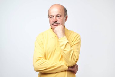Düşünme ve şaşkın bakıyor Sarı tişörtlü rahat olgun adam portresi.