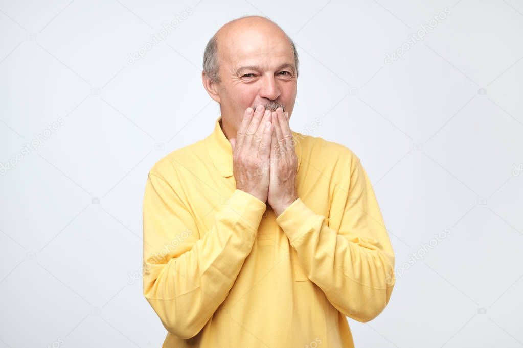Mature bald man covering mouth and laughing.