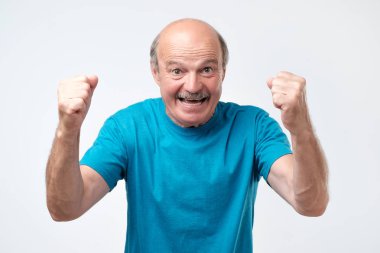 Üst düzey kel adam neşeli ellerini havaya atar.