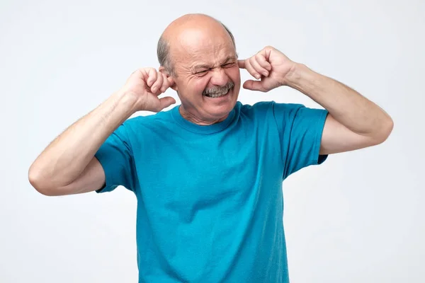 Senior łysy facet hiszpanin zatykanie uszu palcami słuchu wydaje zbyt głośne dźwięki muzyki — Zdjęcie stockowe