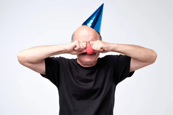 Uomo anziano in cappello di compleanno piangendo e asciugando lacrime sulla sua festa — Foto Stock