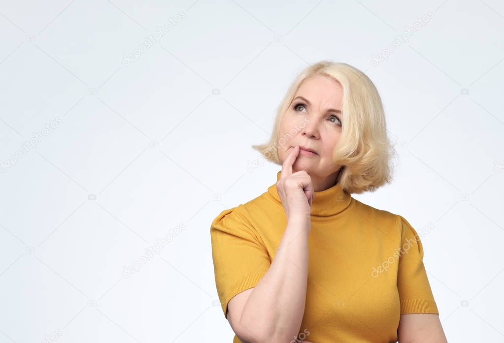 Senior woman looking confident up with smile with hand raised on chin.