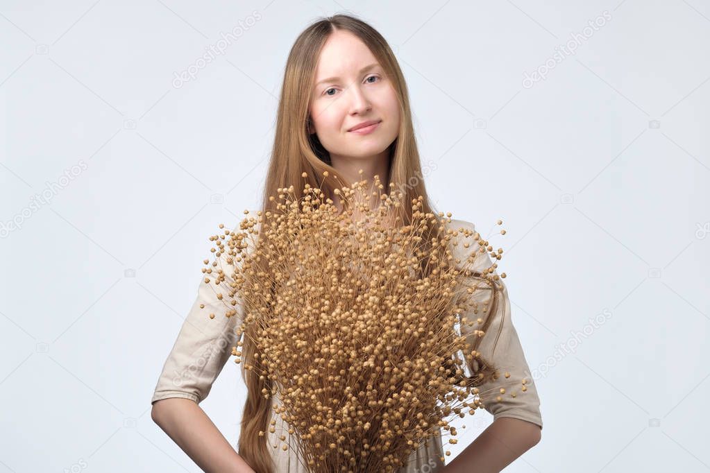 beautiful european woman with long hair holding bouquet of dry flowers of flax.