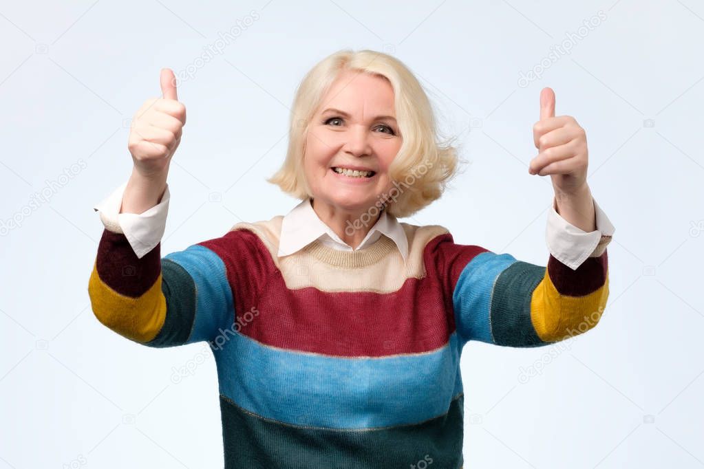 cheerful old woman in colored sweater showing thumbs up gesture